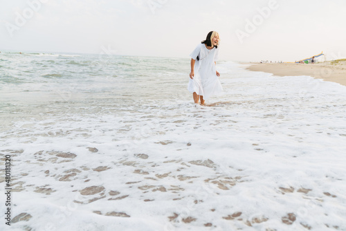 Young asian woman wearing dress laughing while walking on beach