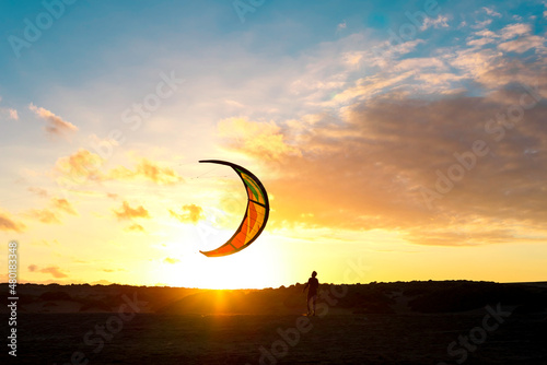 Kitesurfer is catching his kite after training on water. The sunset sun behind, backlight scene.