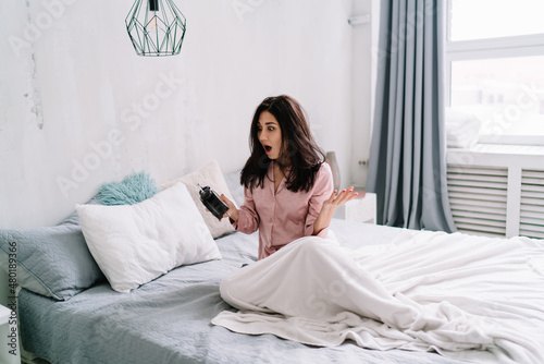 Girl looking time on alarm clock on bed at morning