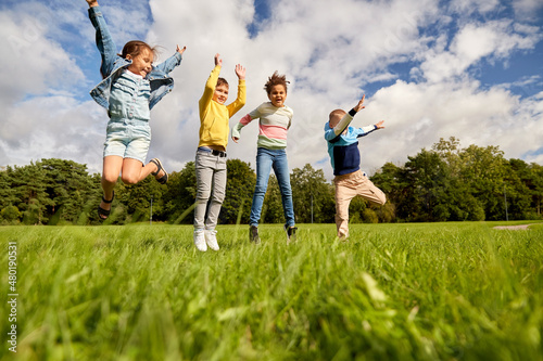 childhood, leisure and people concept - group of happy kids playing and jumping at park
