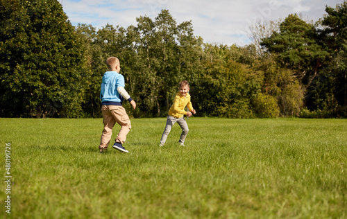 childhood, leisure and people concept - happy boys playing tag game and running at park