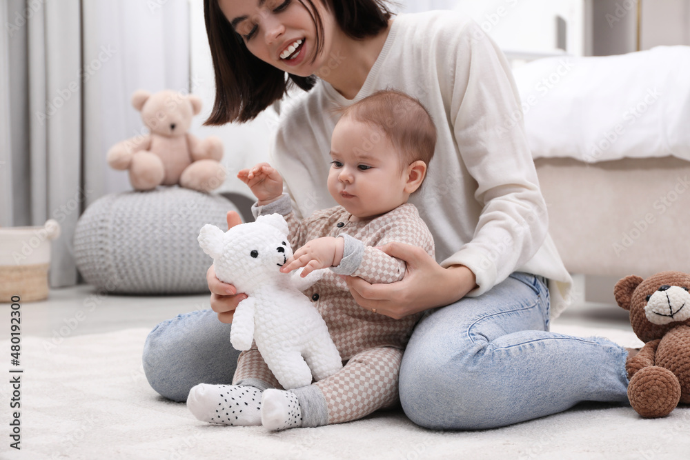 Cute baby and mother playing with toy bear on floor at home Cute baby and mother playing with toy bear on floor at home