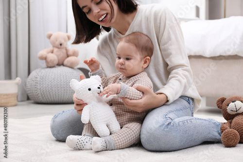 Cute baby and mother playing with toy bear on floor at home