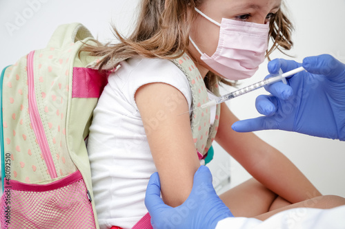 Criança sendo vacinada contra covid 19 volta as aulas medica com luva azul e seringa.
 photo
