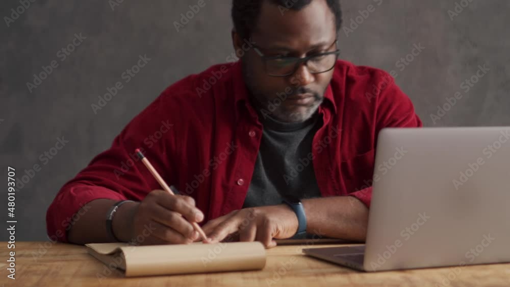 Concentrated African man writing something from laptop in office Concentrated African man writing something from laptop in office