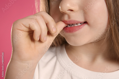 Little girl biting her nails on pink background  closeup