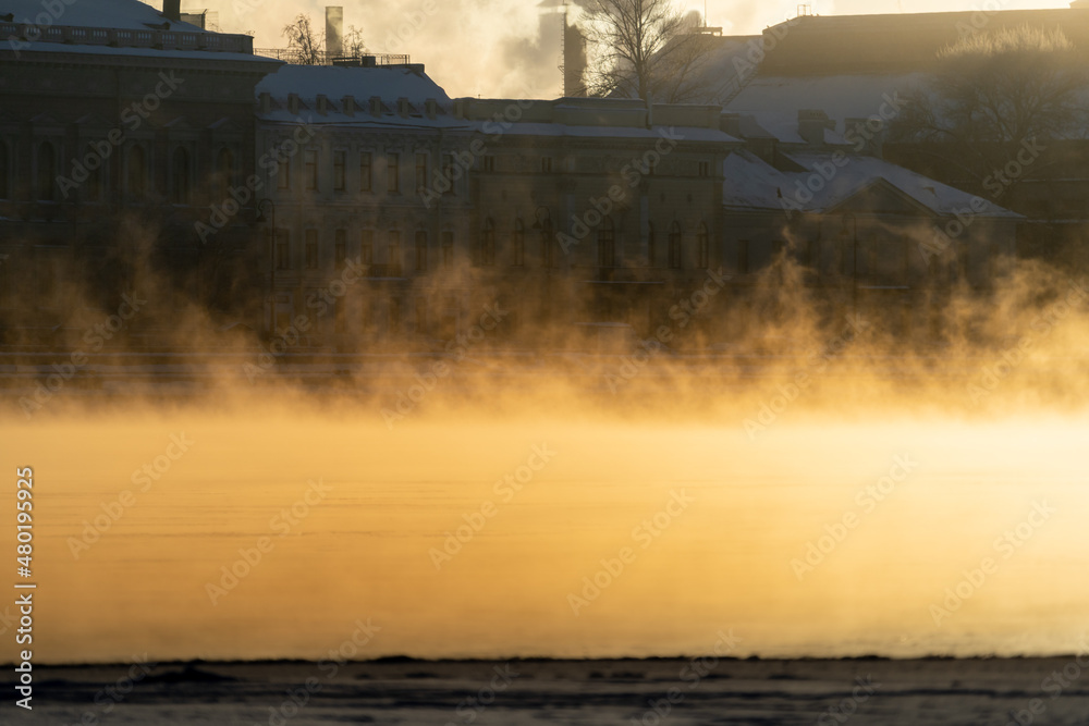 Steam comes out of the river in the city, soaring from the severe cold. Fog in frost winter weather at sunlight. 