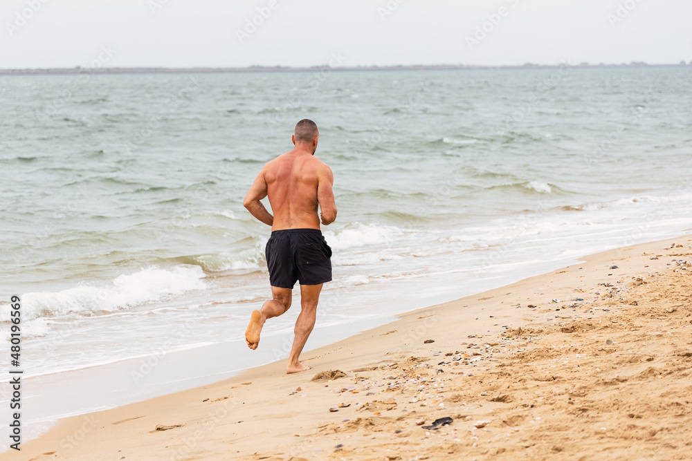 Anonymous shirtless sportsman running on beach Anonymous shirtless sportsman running on beach