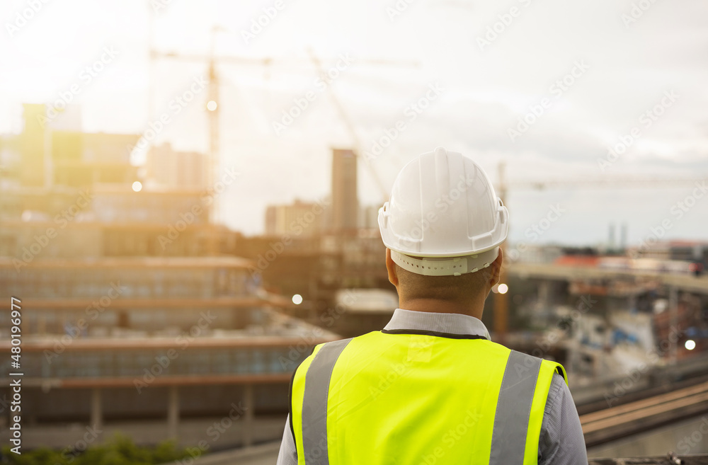 Asian engineer man or architect looking forward with white safety helmet in city construction site . Standing on rooftop building construction at capital. Asian engineer man or architect looking forward with white safety helmet in city construction site . Standing on rooftop building construction at capital.