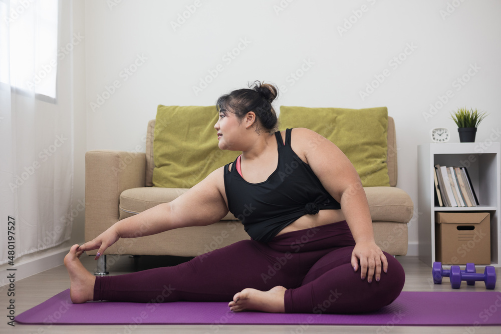 Attractive asian young fitness woman plus size stretching legs warming up before workout at home. Beautiful smiling Female wearing sportswear exercise training yoga in living room.