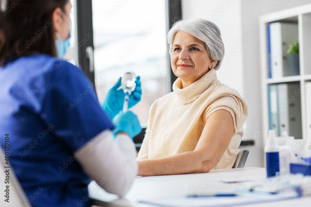 Obraz premium medicine, health and vaccination concept - doctor or nurse filling syringe with vaccine or drug and senior woman at hospital