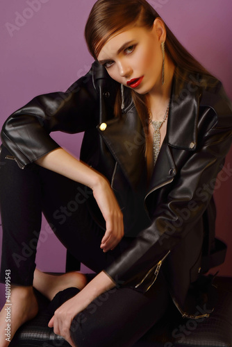A young girl poses in a black leather jacket.