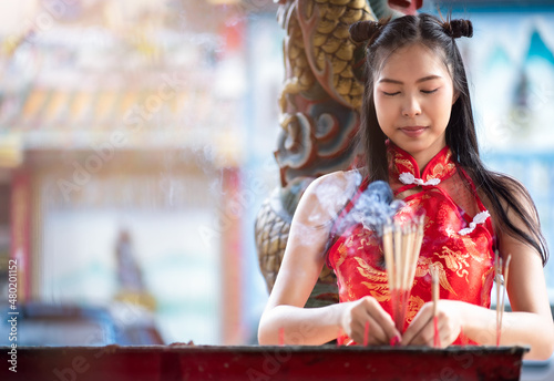 Asian woman in chinese dress traditional cheongsam holding incense pay homage to Chinese god at shrine. Chinese New Year Festival Concept.