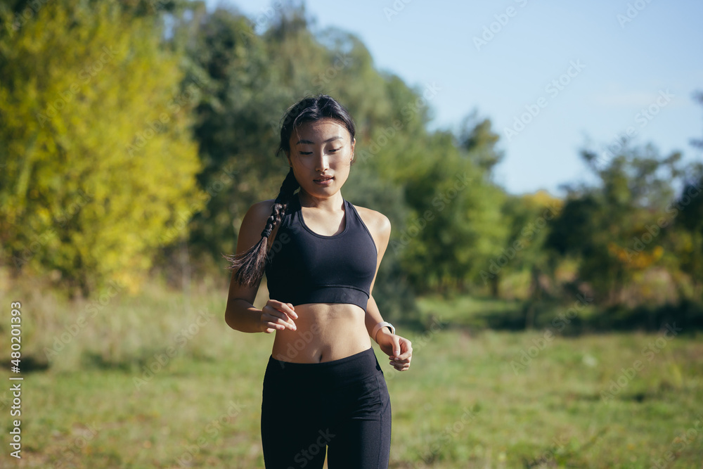 Beautiful Asian woman running in the morning in the park, a woman dressed in a dark sports suit Beautiful Asian woman running in the morning in the park, a woman dressed in a dark sports suit