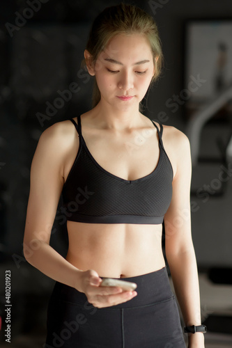 Beautiful smiling woman using a phone while in a gym, Fitness and technology concept .