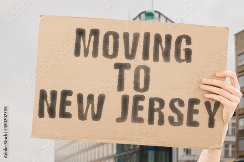 The phrase   Moving to New Jersey   on a banner in men s hand with blurred sea on the background. Relocation. Beach. Sun. Relax. Warm. Apartment. Relocating. Traveler