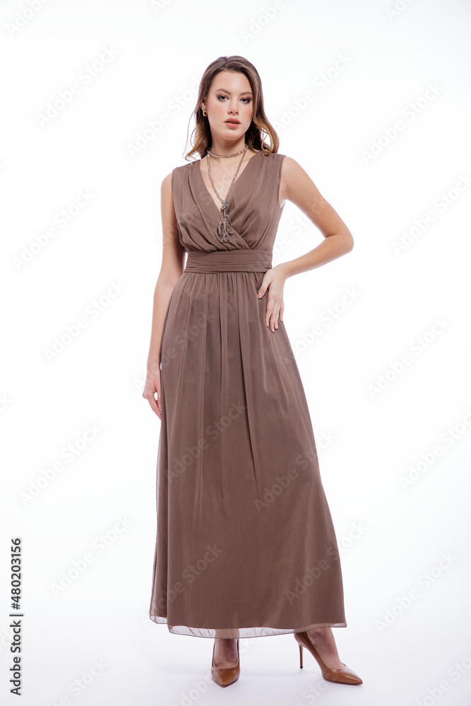 High fashion photo of beautiful elegant young woman in a pretty beige brown dress with a neckline, necklace posing on white background. Slim figure, make up, luxurious hair, shiny curls. Studio Shot High fashion photo of beautiful elegant young woman in a pretty beige brown dress with a neckline, necklace posing on white background. Slim figure, make up, luxurious hair, shiny curls. Studio Shot