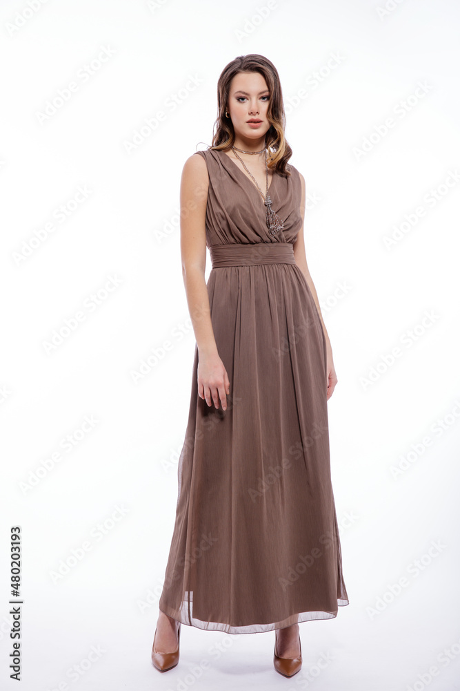 Fototapeta premium High fashion photo of beautiful elegant young woman in a pretty beige brown dress with a neckline, necklace posing on white background. Slim figure, make up, luxurious hair, shiny curls. Studio Shot