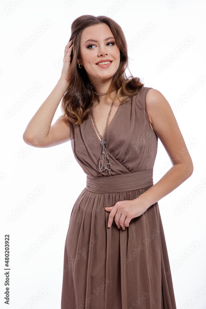 High fashion photo of beautiful elegant young woman in a pretty beige brown dress with a neckline, necklace posing on white background. Slim figure, make up, luxurious hair, shiny curls. Studio Shot High fashion photo of beautiful elegant young woman in a pretty beige brown dress with a neckline, necklace posing on white background. Slim figure, make up, luxurious hair, shiny curls. Studio Shot