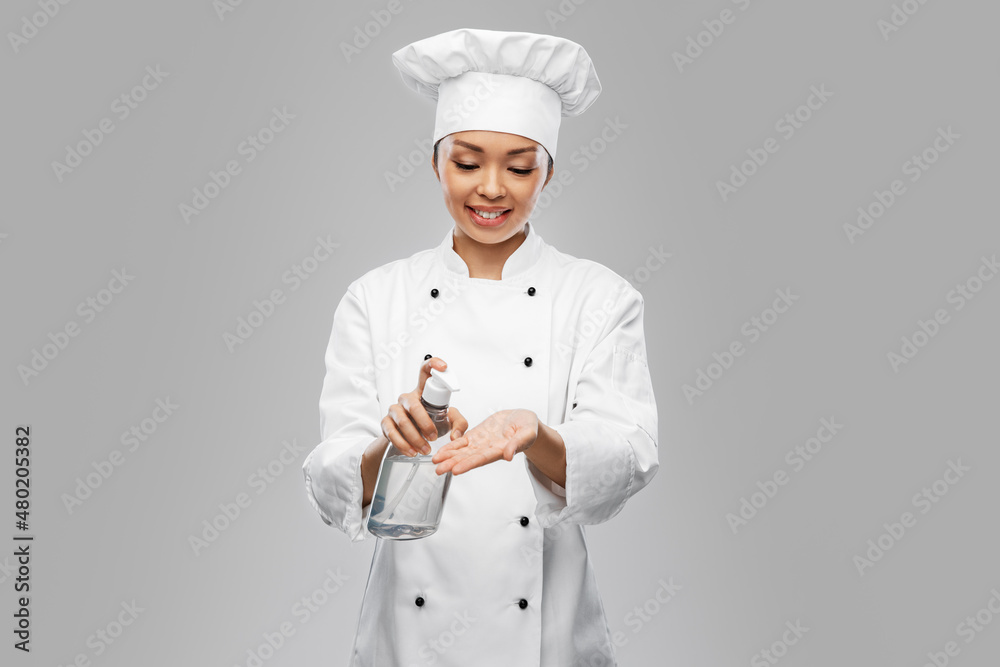 cooking, culinary and people concept - happy smiling female chef in toque applying hand sanitizer or liquid soap over grey background cooking, culinary and people concept - happy smiling female chef in toque applying hand sanitizer or liquid soap over grey background