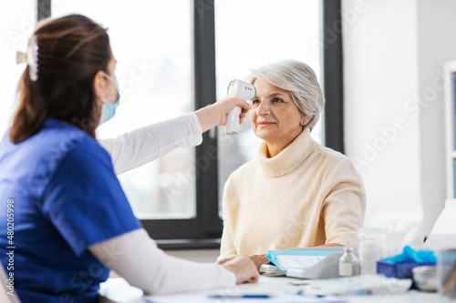 medicine, health and people concept - doctor with infrared thermometer gun checking senior woman's temperature at hospital