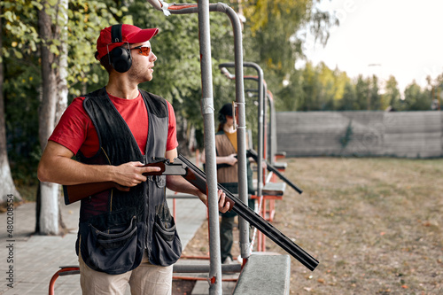 Side View On Focused Male In Outdoor Range, Looking At Side At Target, After Shooting, Concentrated on Training, At Summer Season, Wearing Protective Equipment Uniform, Goggles And Headset
