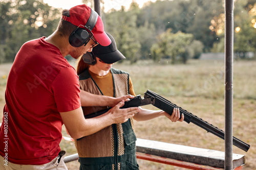 confident caucasian man and young woman checking details of weapon before training loading gun outdoors, sport shooting. trainer and female going to practice shooting together in polygon