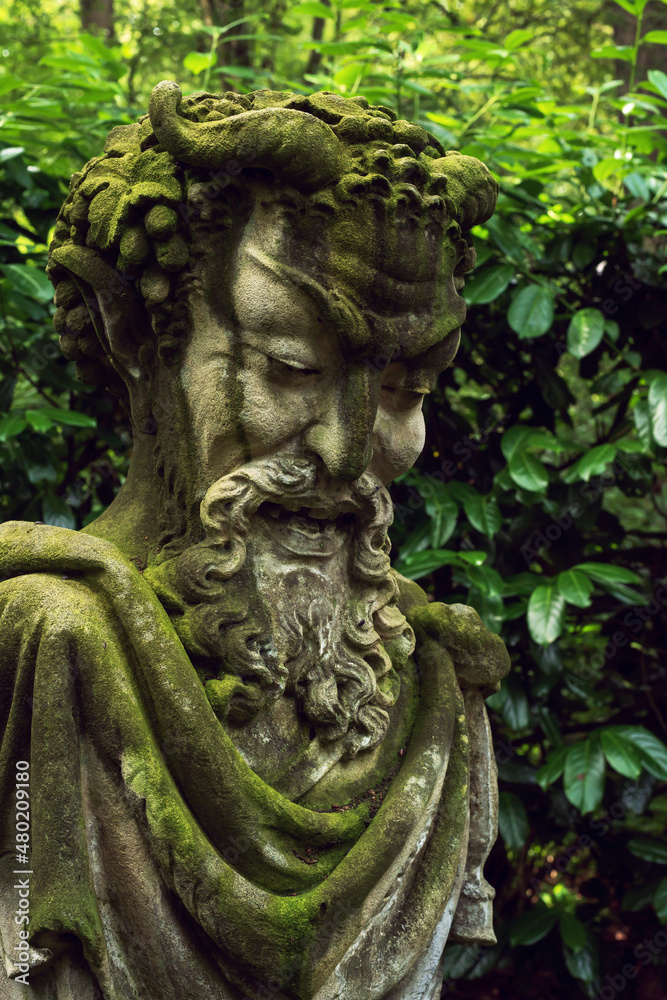 Stone garden statue of a male mythical head in a lush backyard.