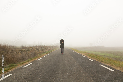 Chica con frío con abrigo caminando con niebla por una carretera secundaria,  huida  © Imagen Punto de Luz