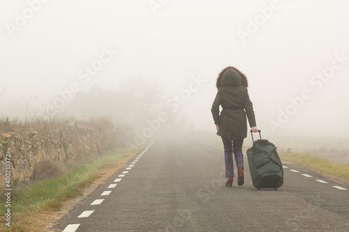 Quadro su tela Con una bolsa maleta una mujer camina por la carretera con mucha niebla, parte t