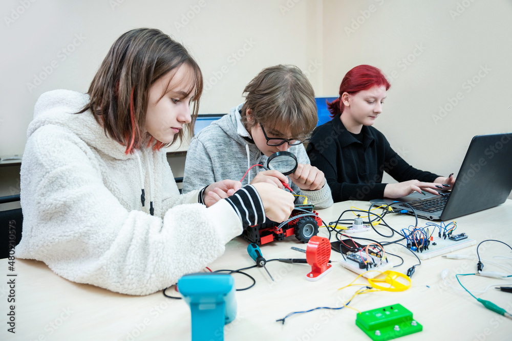 Diverse teenager pupils build robot, learn at table at STEM engineering science education class.