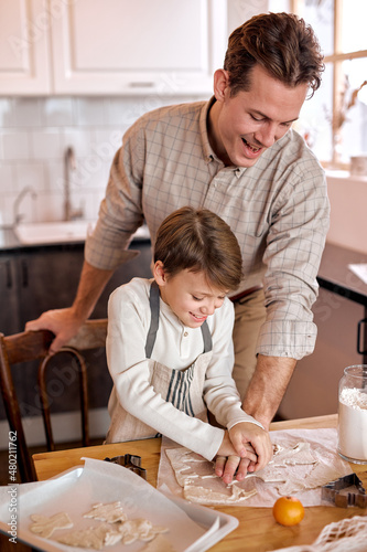 caucasian family having fun prepare bakery cookies together at home. handsome father and adorable son in modern bright kitchen. young Man support little boy, enjoy making xmas cookies