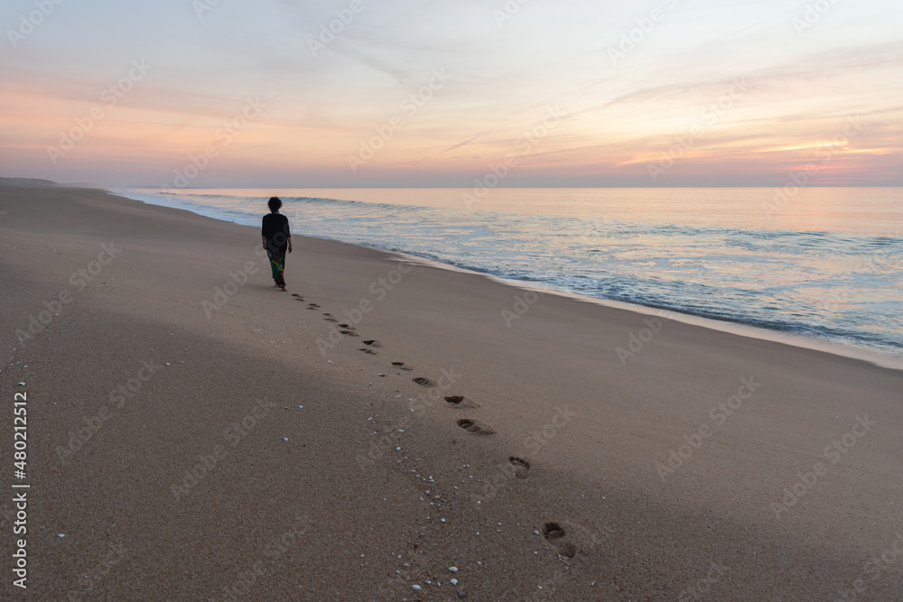 Woman walking at dusk on a beach in Alentejo leaves her footprints on the sand Woman walking at dusk on a beach in Alentejo leaves her footprints on the sand