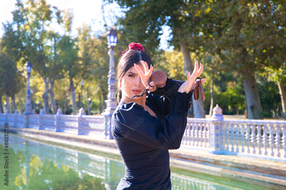 Woman dancing flamenco with black gypsy costume with yellow polka dots and red flower in her hair and castanets in her hands in seville. Concept of flamenco cultural heritage of humanity.