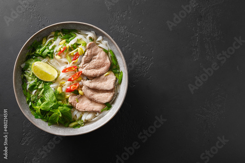 Pho Bo Soup with beef, rice noodles, lime, chili pepper in gray bowl isolated on black background. Popular Vietnamese and Pan-Asian cuisine.