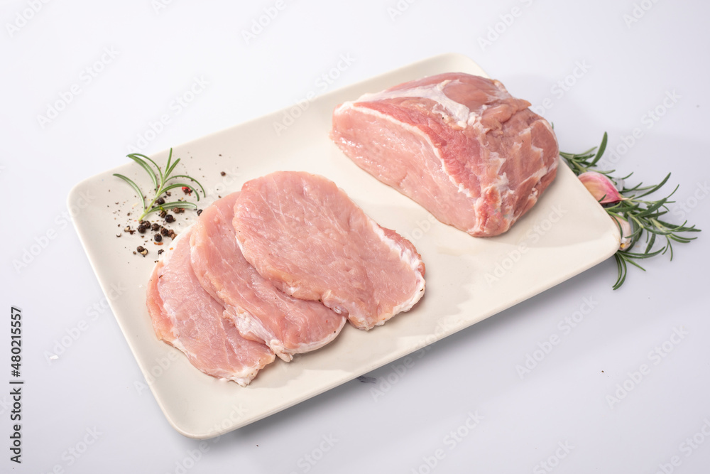 Raw pork meat, loin, ham in chops and in cross-section on a white plate, on white background, top view. Packshot photo.