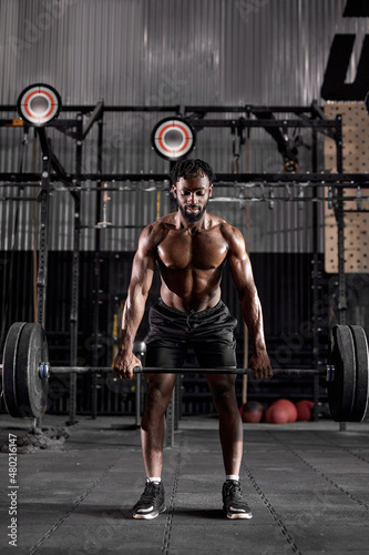 Young muscular african sweaty fit man with big muscles training with heavy barbell weight during cross training workout in modern gym. handsome guy is engaged in sport, fitness, pumping arm muscles