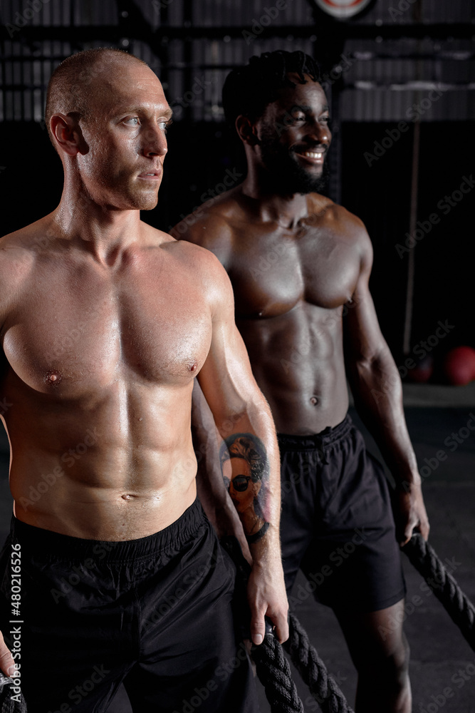 young men black and caucasian preparing for training with cross fit ropes, muscular fit males stand getting ready, looking confident and powerful. sport, fitness, cross fit. focus on white man