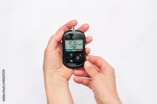 Close-up of the hands of a woman using a glucose meter to measure blood sugar isolated on a white background. Checking blood sugar level by glucometer for diabetes testing. Health care. Top view photo