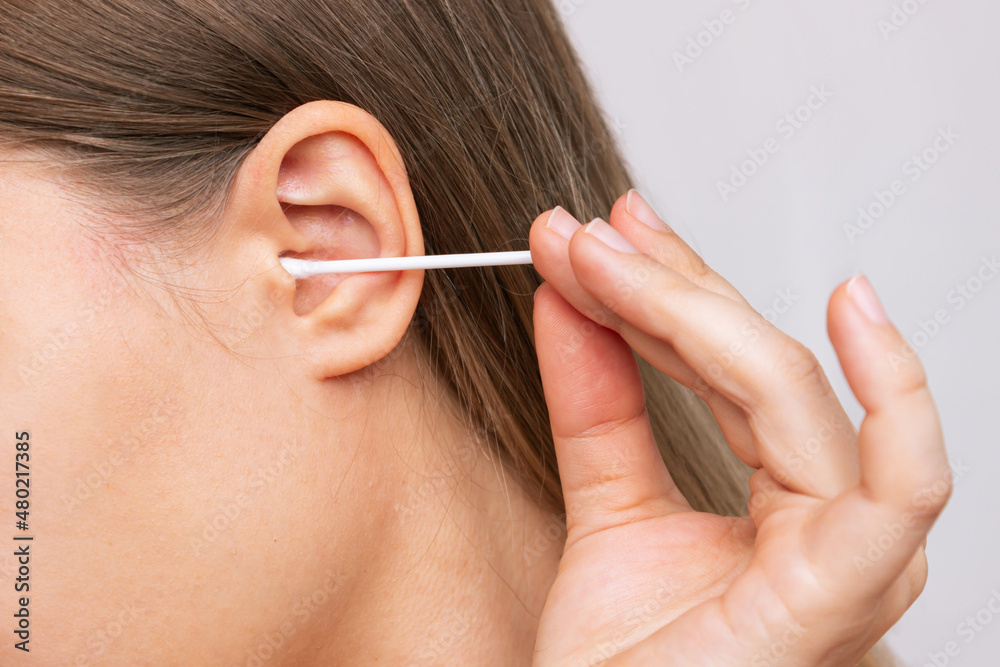 Obraz premium Cropped shot of a young caucasian woman cleaning her ear with a cotton swab isolated on a white background. Hygiene and health care concept