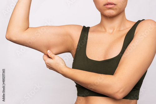 Cropped shot of a young caucasian woman grabbing skin on her upper arm with excess fat isolated on a white background. Pinching the loose and saggy muscles. Overweight concept photo