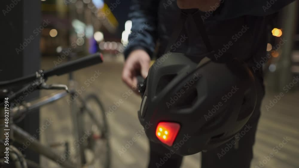 Male cyclist in protective medical mask against air pollution, smog, viruses, infection and allergies puts on bicycle helmet with red lamp at night in city takes bike from parking lot after work. Male cyclist in protective medical mask against air pollution, smog, viruses, infection and allergies puts on bicycle helmet with red lamp at night in city takes bike from parking lot after work.