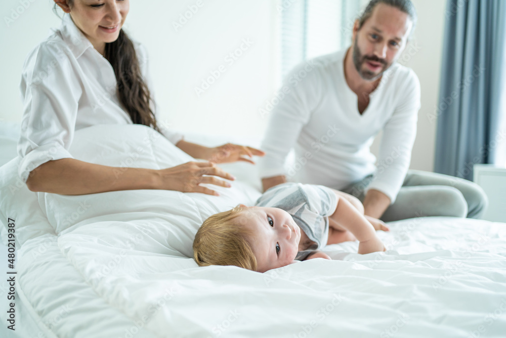 Caucasian parents playing with cute baby boy child on bed in bedroom. Caucasian parents playing with cute baby boy child on bed in bedroom.