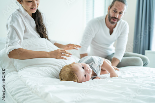 Caucasian parents playing with cute baby boy child on bed in bedroom. 