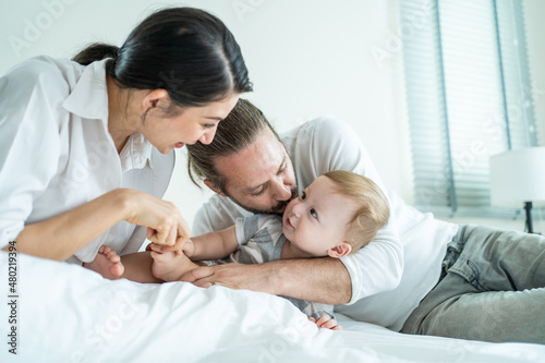 Caucasian parents playing with cute baby boy child on bed in bedroom.