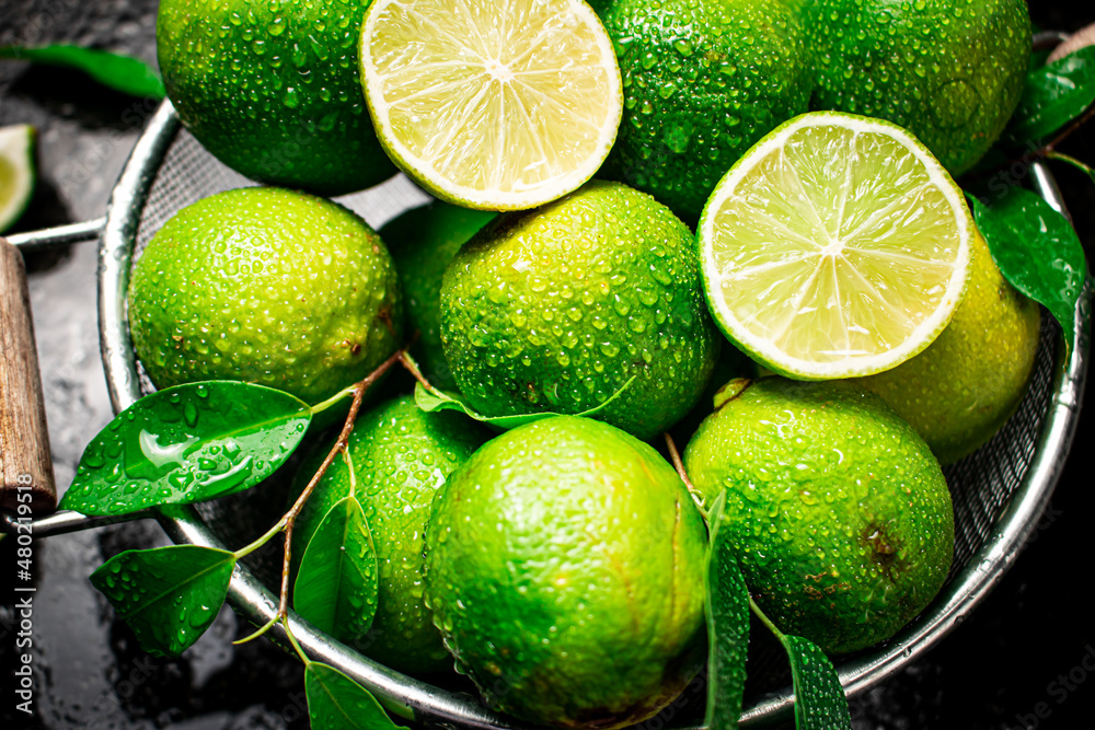 Fragrant lime with leaves in a colander. On a black damp background. High quality photo - obrazy, fototapety, plakaty 