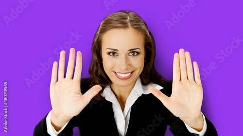 Portrait of happy smiling young business woman in black suit showing stop gesture, isolated over purple violet background. Cheerful busiesswoman showing holding raising open hands, palms. photo