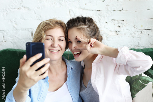 Fototapeta Naklejka Na Ścianę i Meble -  Portrait of beautiful mature mother and her daughter making a selfie using smart phone and smiling, home and happy.