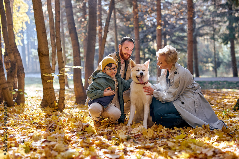 Young caucasian family with pet dog relax while walking in park, on autumn season, attractive female, handsome guy and cute child boy with pet have fun, rejoicing, experiencing positive emotions