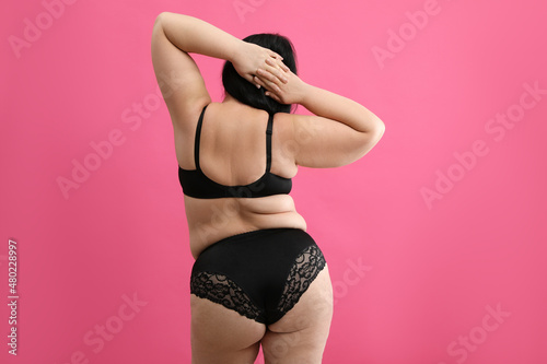 Back view of beautiful overweight woman in black underwear on pink background. Plus-size model